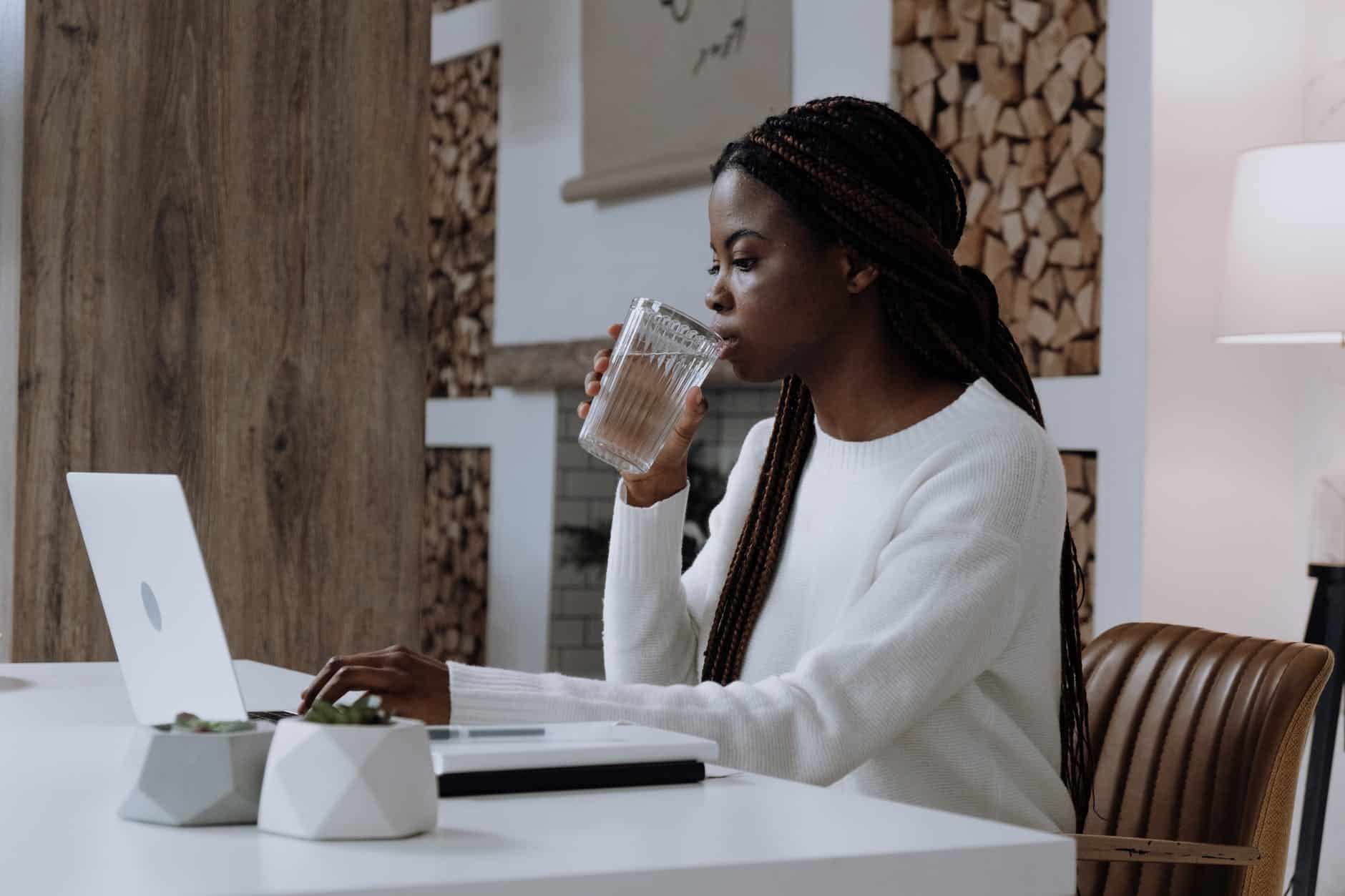 woman drinking water while working on laptop